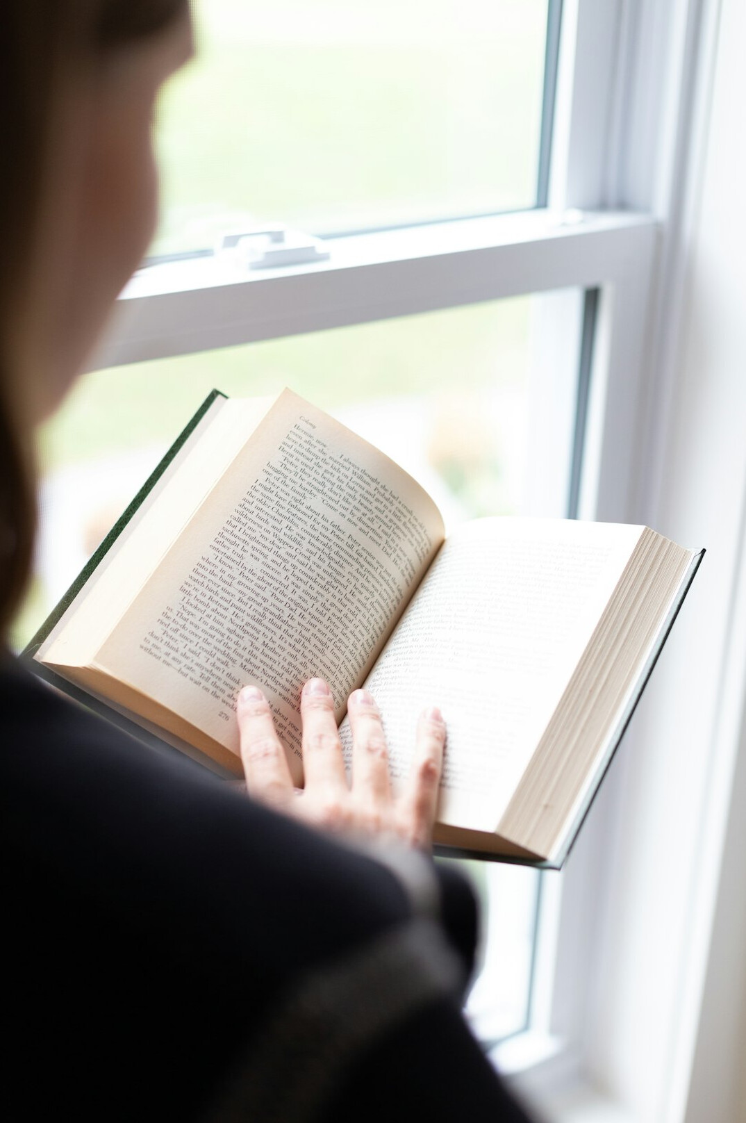 Person reading a book by a window, reflective mood